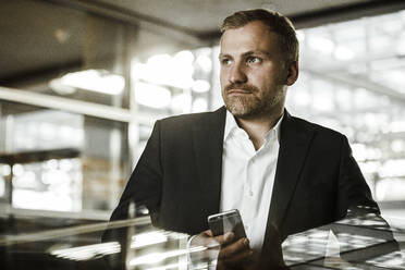 Portrait of businessman with smartphone looking sideways - SAJF00077