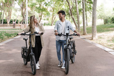 Smiling young couple with electric bicycles walking on road - RDGF00109