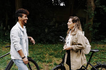 Happy boyfriend and girlfriend talking while standing by electric bicycles - RDGF00121