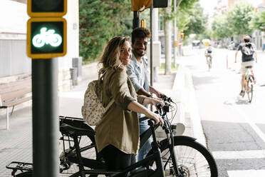 Smiling young couple with electric bicycles standing on sidewalk - RDGF00124