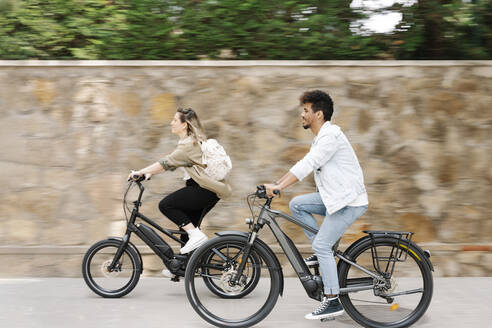Couple riding electric bicycles on road in city - RDGF00127