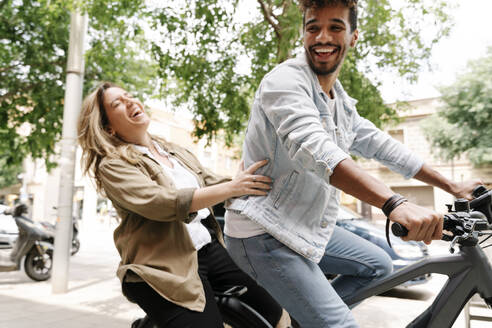 Fröhliches junges Paar genießt Fahrt auf elektrischem Fahrrad in der Stadt - RDGF00128
