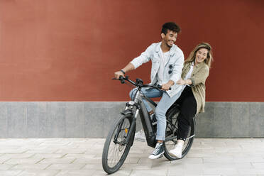Happy couple enjoying ride on electric bicycle in city - RDGF00129