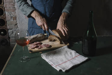 Mittelteil eines Mannes beim Schneiden von selbstgebackenem Brot auf einem Brett am Tisch - ALBF01413