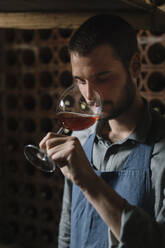 Young man tasting wine from glass in cellar - ALBF01416
