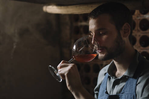 Junger bärtiger Mann trinkt Wein aus einem Glas im Keller - ALBF01417