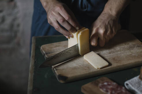 Hände eines Mannes, der handwerklich hergestellte Käsescheiben auf einem Brett am Tisch schneidet - ALBF01419