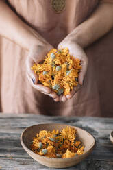 Frau mit verschränkten Händen, die frische orangefarbene Blumen über einer Schale auf dem Tisch hält - ALBF01428