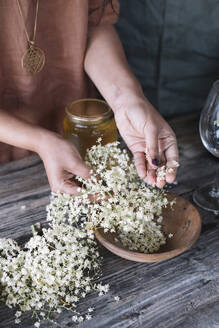 Midsection of woman preparing fresh cocktail with white flowers on wooden table - ALBF01445