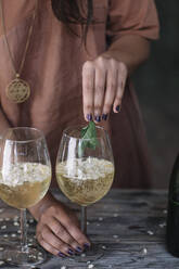 Midsection of woman holding mint leaves over wineglass while preparing cocktail - ALBF01453