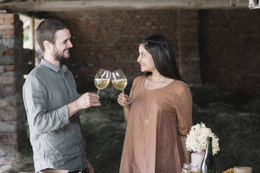 Happy couple toasting cocktail while looking at each other in barn - ALBF01458