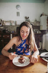Beautiful woman having slice of cake at home - LJF01748