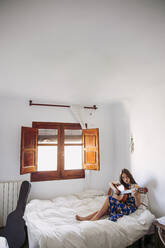 Junge Frau übt Gitarre, während sie zu Hause auf dem Bett sitzt - LJF01756