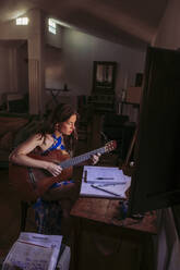 Junge Frau übt Gitarre im Wohnzimmer zu Hause - LJF01768