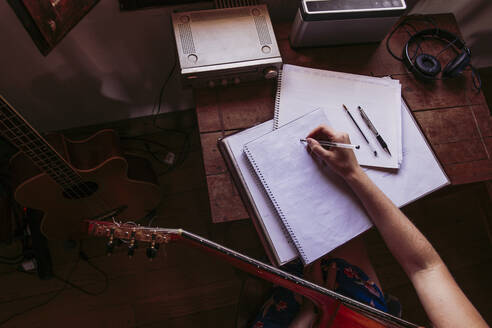 Junge Frau schreibt in ein Buch, während sie zu Hause Gitarre übt - LJF01778
