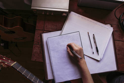 Junge Frau schreibt am Tisch in ein Buch, während sie Gitarre übt - LJF01780