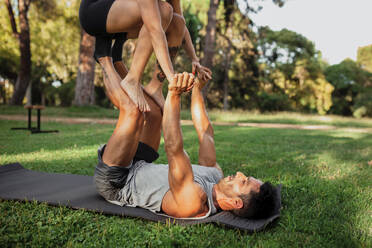 Lying on yoga mat young Woman holding muscular man on lifting legs