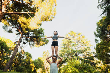 Young woman standing on shoulders of boyfriend while practicing acroyoga - MRRF00348