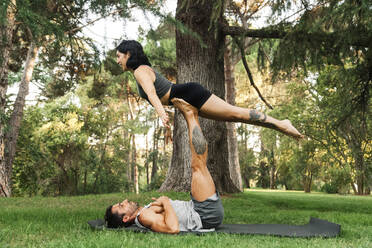 Mann balanciert seine Freundin auf den Beinen, während er im Park Acroyoga übt - MRRF00352