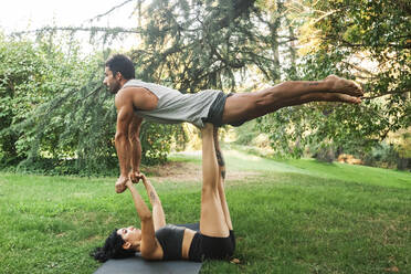 Female athlete balancing boyfriend on legs while holding hands in park - MRRF00353