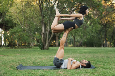 Man balancing girlfriend on legs while doing acroyoga in park - MRRF00357