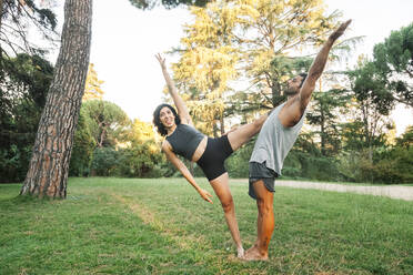 Couple stretching while doing acroyoga in public park - MRRF00358