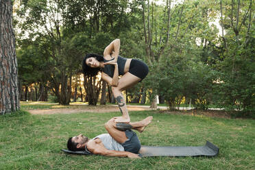Mann balanciert Freundin auf den Beinen, während er Acroyoga im öffentlichen Park praktiziert - MRRF00359