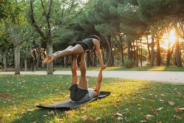 Paar übt Acroyoga im öffentlichen Park bei Sonnenuntergang - MRRF00360