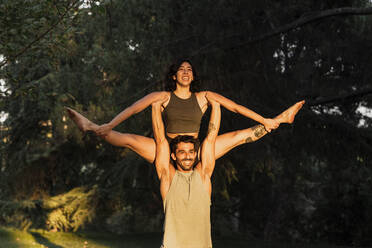 Smiling man lifting woman while practicing acroyoga in public park - MRRF00364