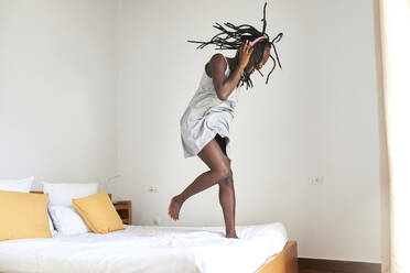 Junge Frau beim Tanzen und Musikhören auf dem Bett zu Hause - KIJF03250