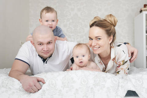 Happy parents with two children lying on bed stock photo