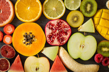 Draufsicht auf verschiedene geschälte und geschnittene gesunde Früchte und Gemüse, die auf einem schwarzen Holztisch angeordnet sind - ADSF12544