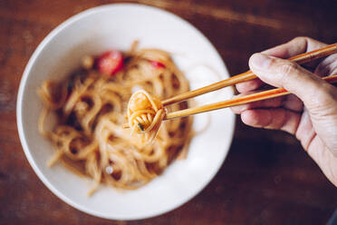 From above soft focus of crop person holding shrimp by wooden chopsticks while enjoying noodles on blurred background - ADSF12556