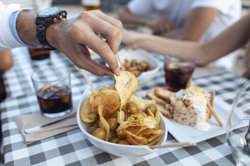 Beschnittenes Bild eines Mannes mit Kartoffelchips in einem Café - JSRF01103