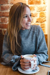Smiling woman holding coffee cup at coffee shop - JMPF00354