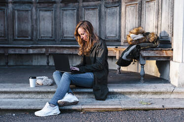 Geschäftsfrau sitzt im Park und arbeitet am Laptop - JMPF00362