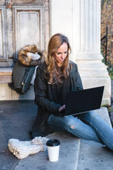 Beautiful businesswoman sitting on steps while laptop in park - JMPF00364