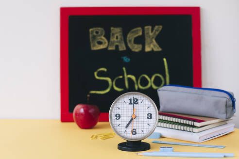 Nahaufnahme eines Weckers mit Schulsachen und Apfel auf dem Tisch - MOMF00904