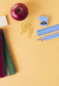 School supplies with fresh apple on yellow table - MOMF00905