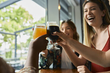 Glückliche Freundinnen stoßen in einer Kneipe mit Craft-Bier-Gläsern an - ZEDF03632