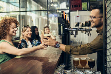 Barkeeper, der einer Frau in einer Kneipe ein Glas Bier überreicht - ZEDF03646