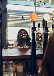 Smiling young woman sitting at the counter in a pub - ZEDF03650