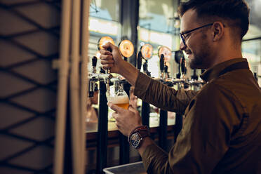 Lächelnder Barkeeper zapft Bier in einer Kneipe - ZEDF03651