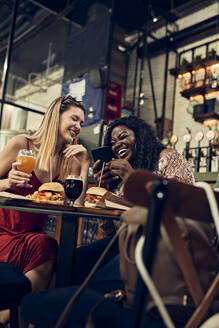 Happy female friends with smartphone having burgers in a pub - ZEDF03660