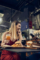 Happy woman with friend in a pub having a beer and a burger - ZEDF03661