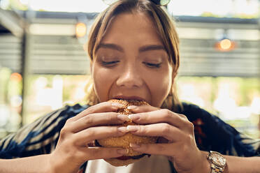 Portrait of woman eating a burger - ZEDF03664