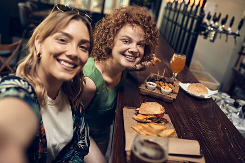 Happy female friends socializing in a pub taking a selfie - ZEDF03670