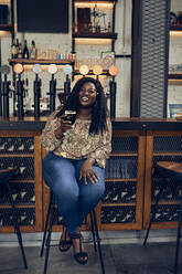 Glückliche Frau sitzt am Tresen in einer Kneipe und trinkt ein Bier - ZEDF03673