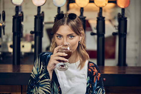 Porträt einer lächelnden Frau in einer Kneipe, die ein Bier trinkt, lizenzfreies Stockfoto