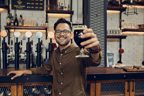 Porträt eines lächelnden Mannes, der sein Bierglas in einer Kneipe hebt - ZEDF03681